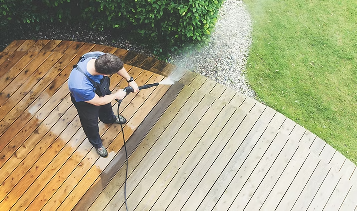 Technician pressure washing a backyard wooden deck, cleaning boards from gray weathering to a brighter wood finish.